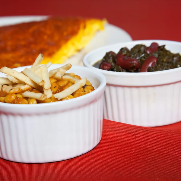 Two white ramekins of Persian stews, one with beans and noodles, on a red tablecloth.