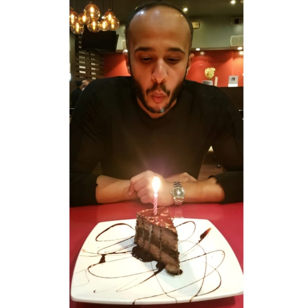 A man blowing out a candle on a slice of chocolate cake at Farsi Cafe.