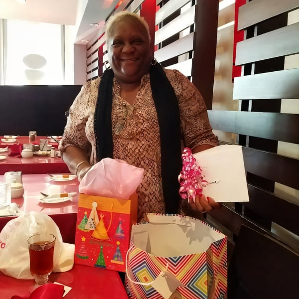Smiling woman holding a gift bag and card at a Farsi Cafe table with red accents.