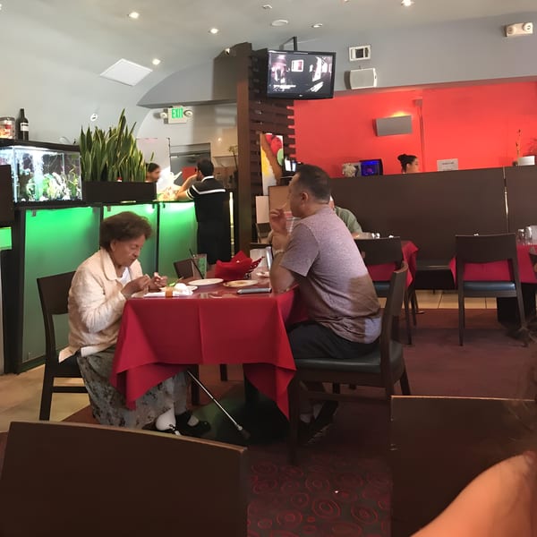 Diners at Farsi Cafe, with an older woman and man seated at a red-clothed table.