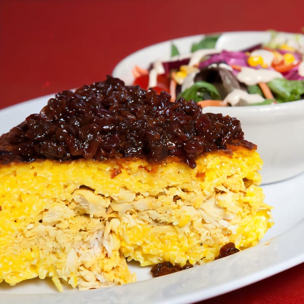 Persian Tahchin with shredded chicken and saffron rice, topped with caramelized onions, served with a side salad.