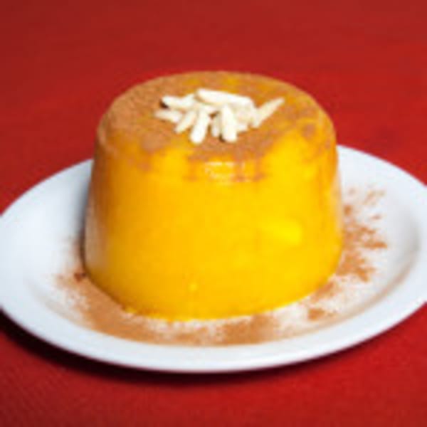 Sholeh Zard, a yellow Persian saffron rice pudding, topped with slivered almonds and cinnamon on a white plate.