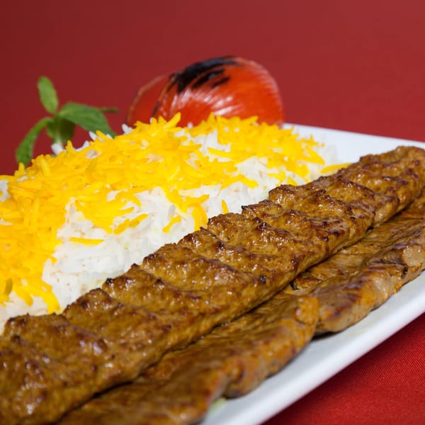 Two skewers of grilled Persian koobideh kebab with saffron rice, a grilled tomato, and mint.