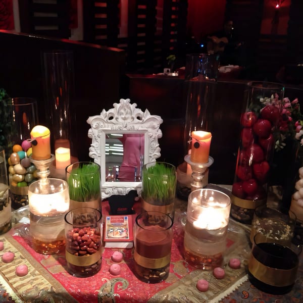 A Haft-Seen table with candles, sprouts, and decorative items, reflecting in a mirror at Farsi Cafe.