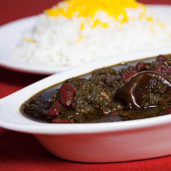 A white bowl of Farsi Cafe's Ghormeh Sabzi, a Persian herb stew with kidney beans, next to rice.