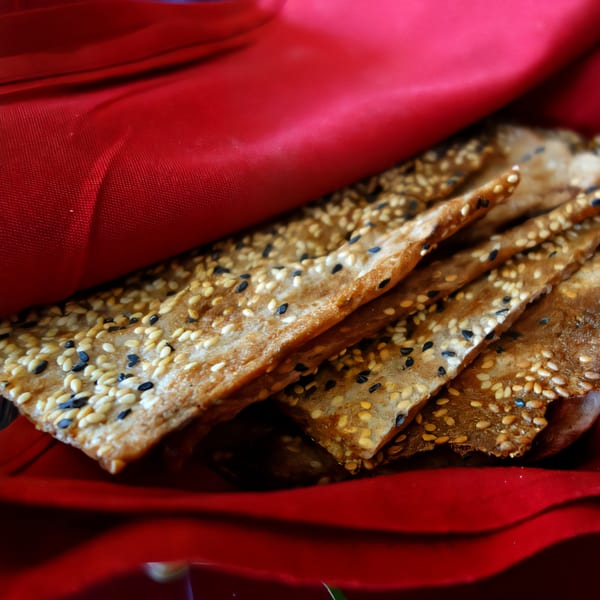 Crispy Persian flatbread with white and black sesame seeds, nestled in a red cloth.