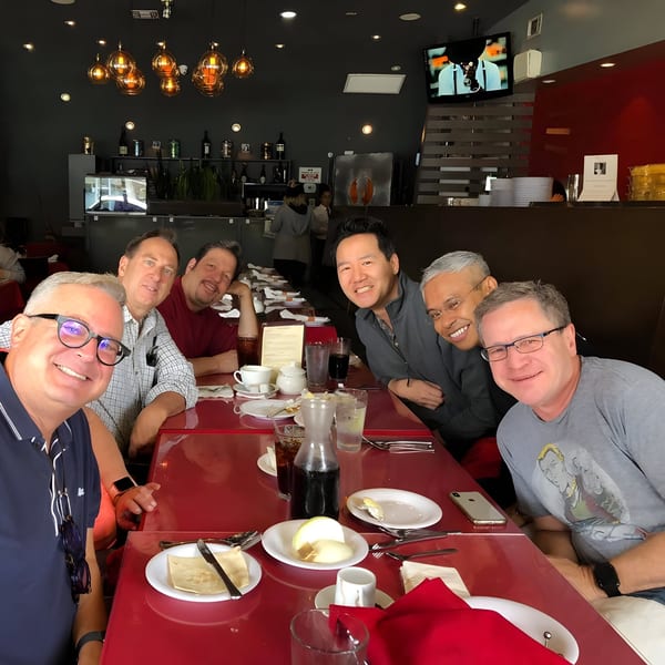 Six men smiling at the camera while sitting around a red table at Farsi Cafe.