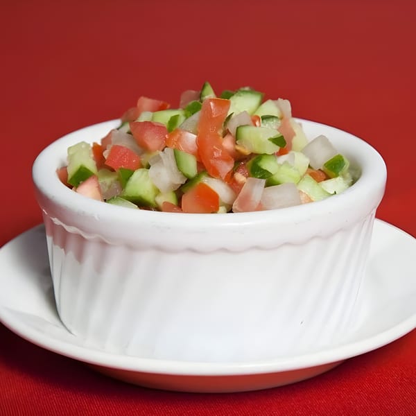 Shirazi salad with diced cucumbers, tomatoes, and onions in a white ramekin on a red background.