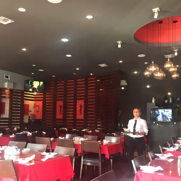 A Farsi Cafe dining room with red tablecloths, dark wood accents, and a server holding a menu.