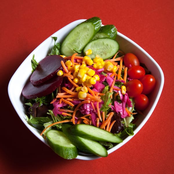 A colorful Farsi Cafe house salad with lettuce, cucumbers, beets, corn, carrots, and cherry tomatoes.